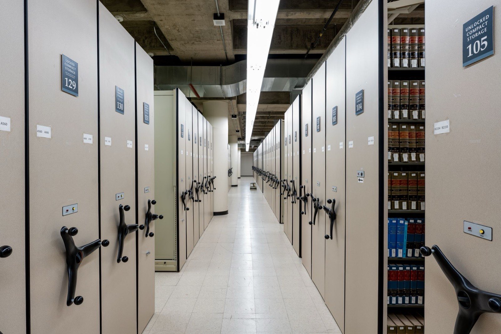 Salle d’archives, rayonnages mobiles alignés sur toute la longueur de la pièce.